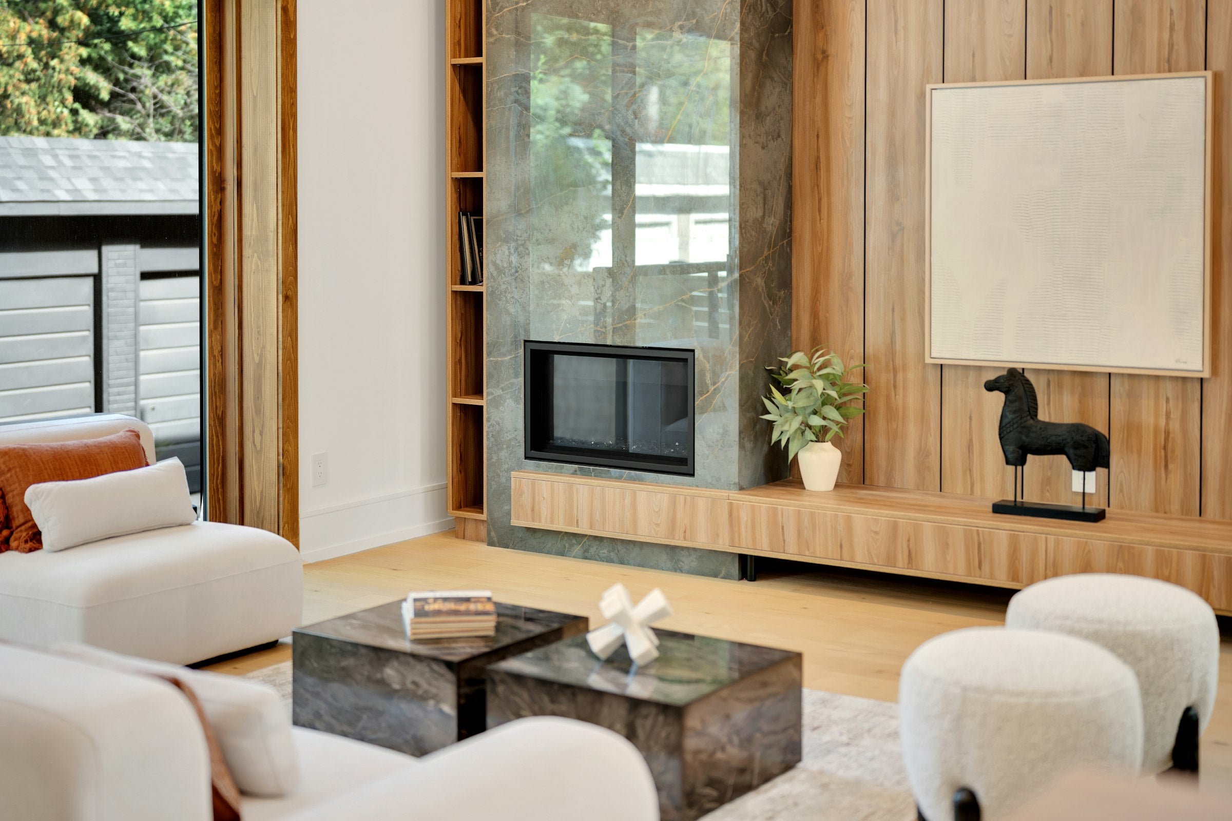 Modern living room with warm wood paneling, marble fireplace, and indoor-outdoor connection